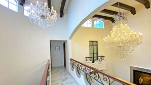 A grand staircase with marble flooring, ornate black iron railings, and two large crystal chandeliers.