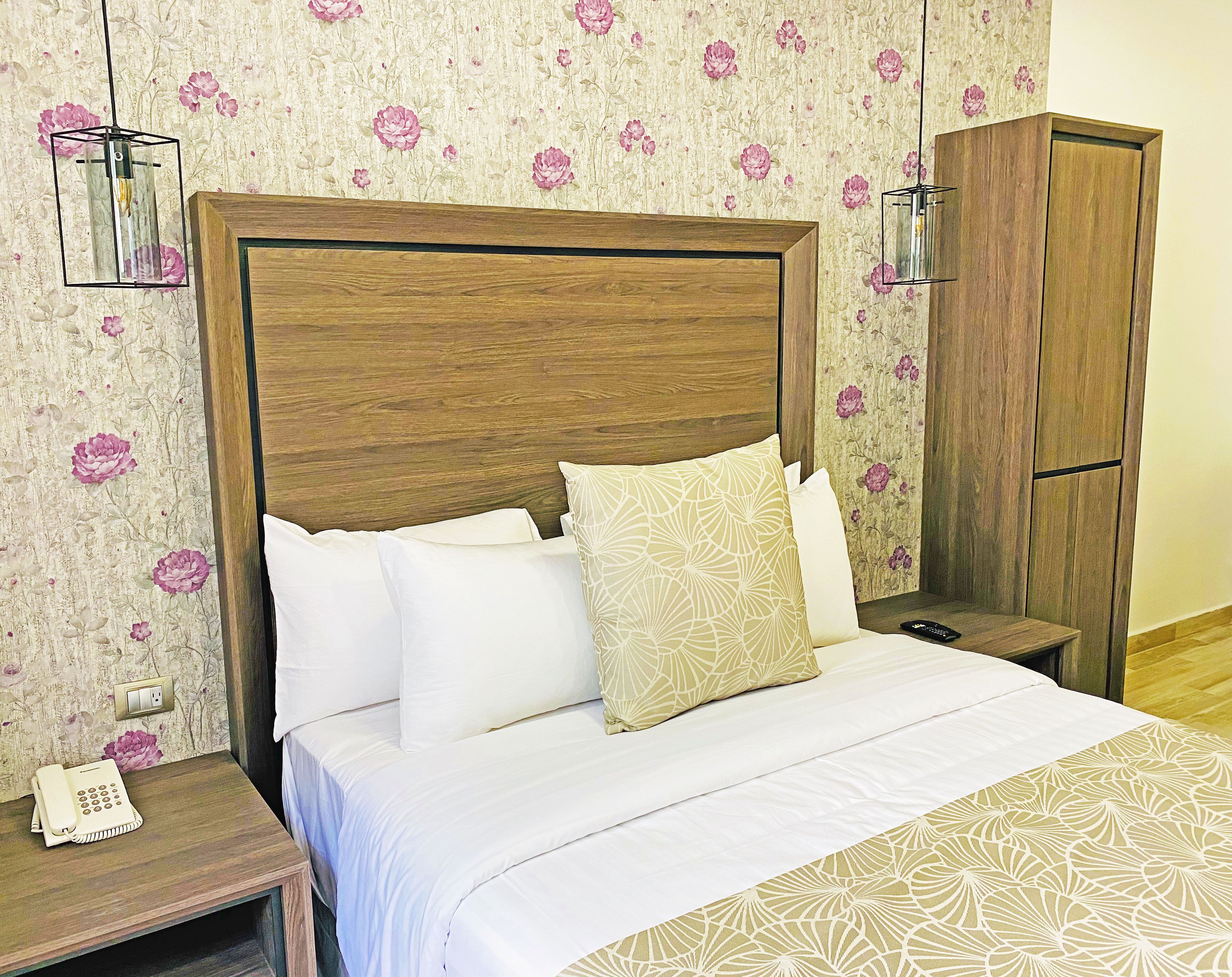 A hotel room with a wooden headboard, a bed with white bedding, a nightstand with a telephone, and a wardrobe.