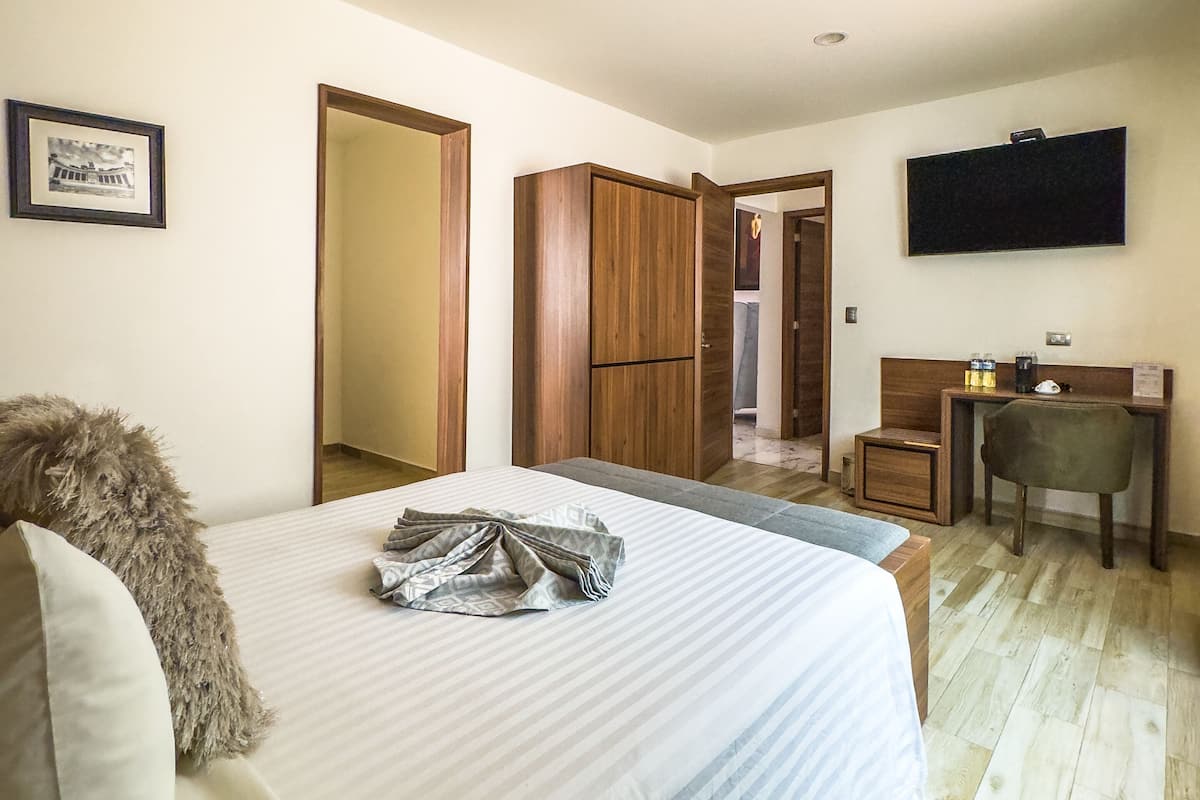 A bedroom with a bed, a desk, a chair, a television, and a wardrobe.