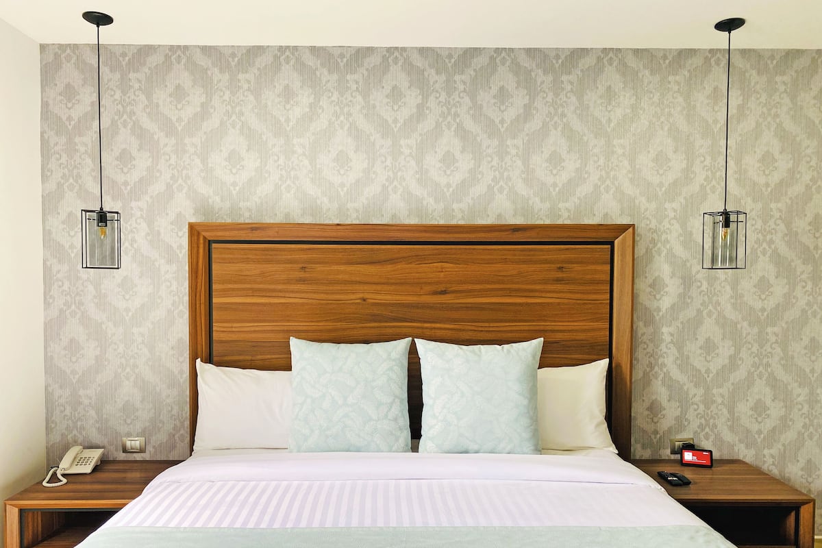 A neatly made bed with a wooden headboard, two bedside tables with lamps, and a patterned wallpaper.