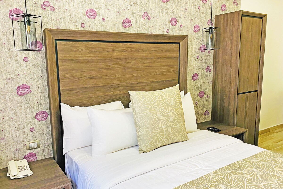 A hotel room with a wooden headboard, a bed with white bedding, a nightstand with a telephone, and a wardrobe.