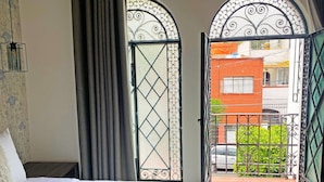 A bedroom with a bed, a window with a decorative iron gate, and a view of the outside balcony.