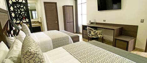 A hotel room with two beds, a desk, a chair, a TV, and a bathroom visible through a door.
