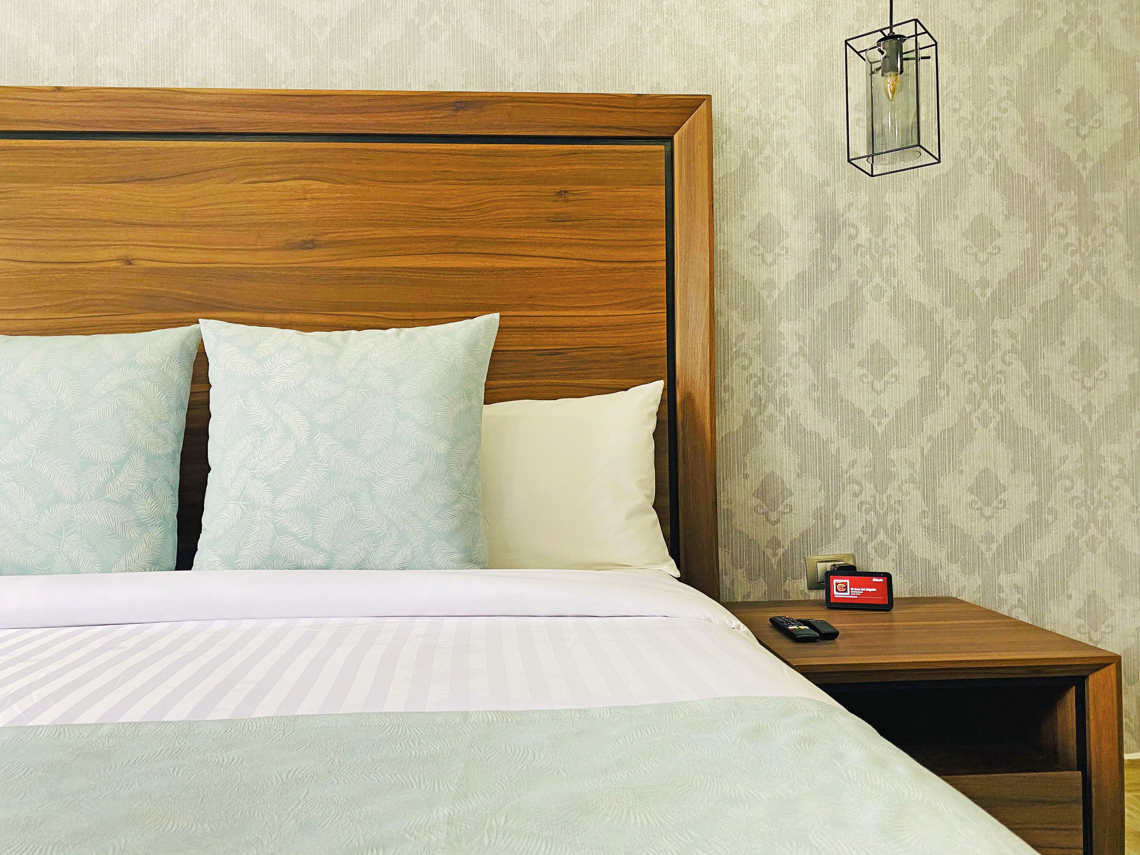 A neatly made bed with a wooden headboard, two pillows, a striped blanket, and a bedside table with a remote control and a clock.