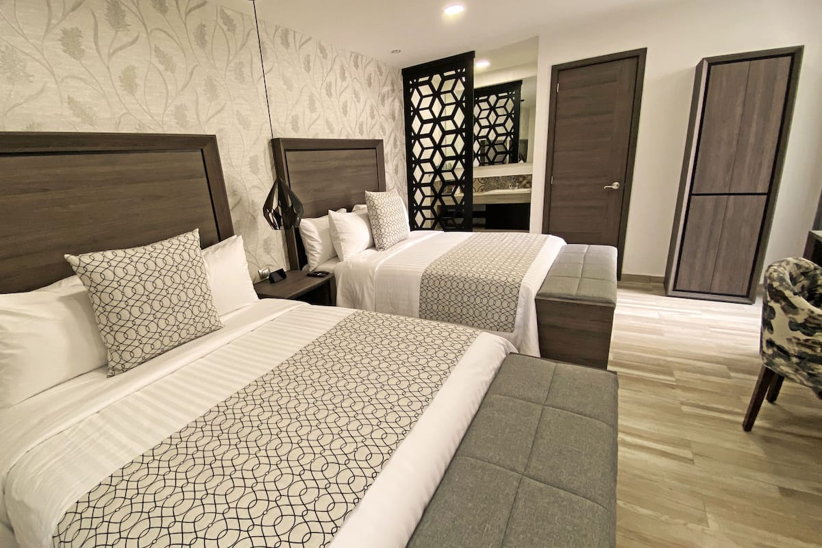 A hotel room with two beds, a wooden headboard, a nightstand, a mirror, and a wardrobe.
