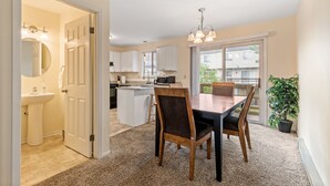 Una cocina moderna con armarios blancos, una isla central y un comedor con mesa y sillas de madera.
