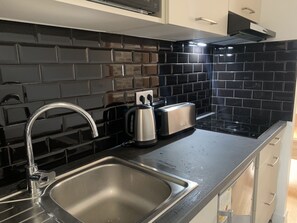 A modern kitchen with a black tiled backsplash, stainless steel sink, and a toaster. - le cottage des remparts - face hôtel de ville (Boulogne-sur-Mer)
