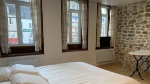 Une chambre à coucher avec un grand lit, trois fenêtres avec des rideaux, un mur en pierre, une petite table et un radiateur.