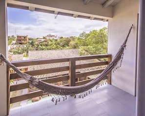 A hammock on a balcony with a view of buildings and trees. - Pousada do Mica (Imbituba)