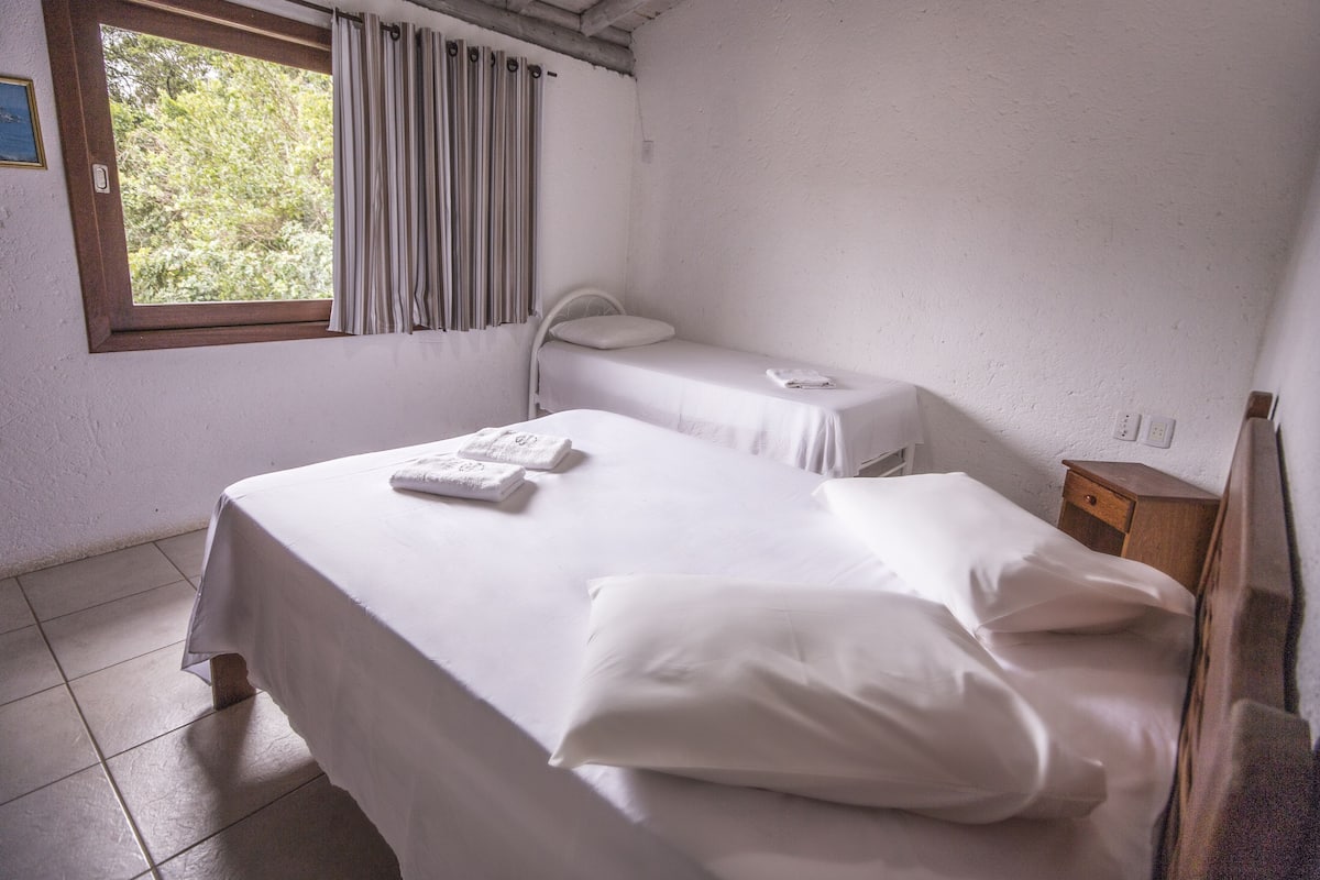 Ein Zimmer mit zwei Betten, einem Fenster mit Vorhängen, einem Nachttisch und einer Steckdose.