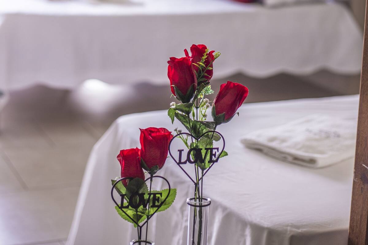 Ein Hotelzimmer mit zwei Betten, einer Vase mit roten Rosen und einem Schild mit der Aufschrift 'LOVE'.