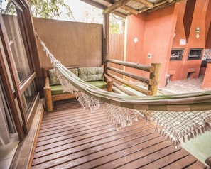 A hammock on a wooden deck with a green cushioned bench and a wooden fence. - Pousada do Mica (Imbituba)