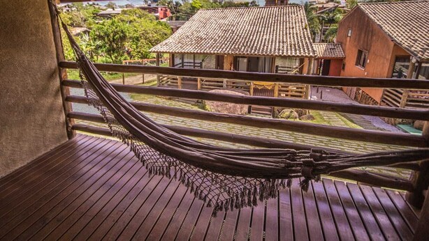 A hammock on a wooden deck with a view of traditional buildings and a clear sky. - Pousada do Mica (Imbituba)