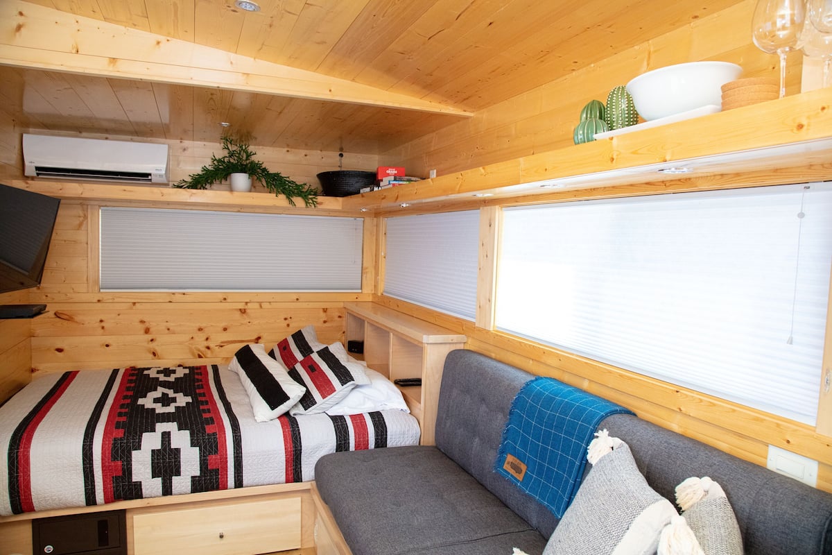 Interior compacto de una caravana con cama, sofá y persianas.