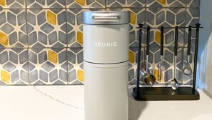 A KEURIG coffee maker on a kitchen counter with a patterned backsplash and a wooden shelf above.