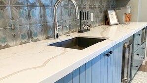 A kitchen with a white marble countertop, a stainless steel sink, and blue cabinets.