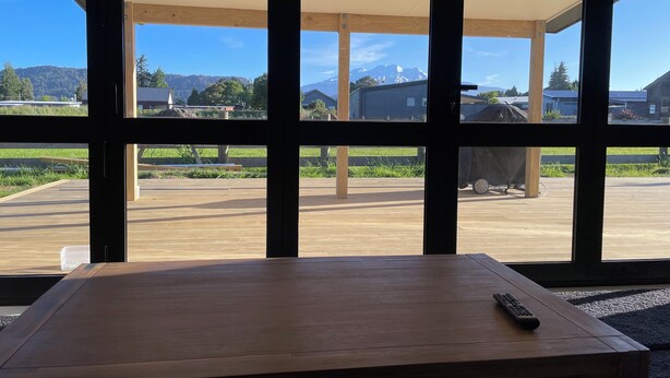 Una habitación con ventanas amplias, una mesa de madera y un control remoto sobre la mesa.