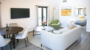 A modern living room with a round dining table, a sofa, a green armchair, and a bed in the background.