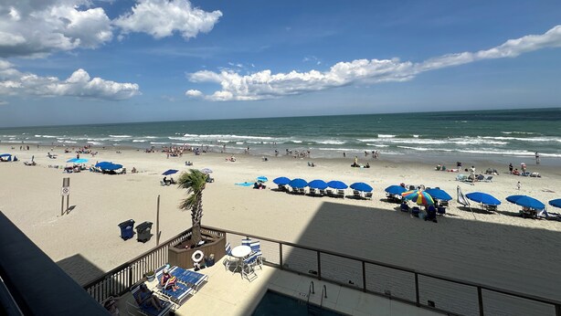 A beach with umbrellas and lounge chairs, a pool area, and a view of the ocean.