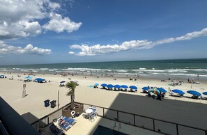 A beach with umbrellas and lounge chairs, a pool area, and a view of the ocean.