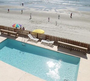 A pool area with lounge chairs and umbrellas, adjacent to a beach with people walking. - Carolina Shores II 1202 - Oceanfront in Garden City Beach (Garden City)