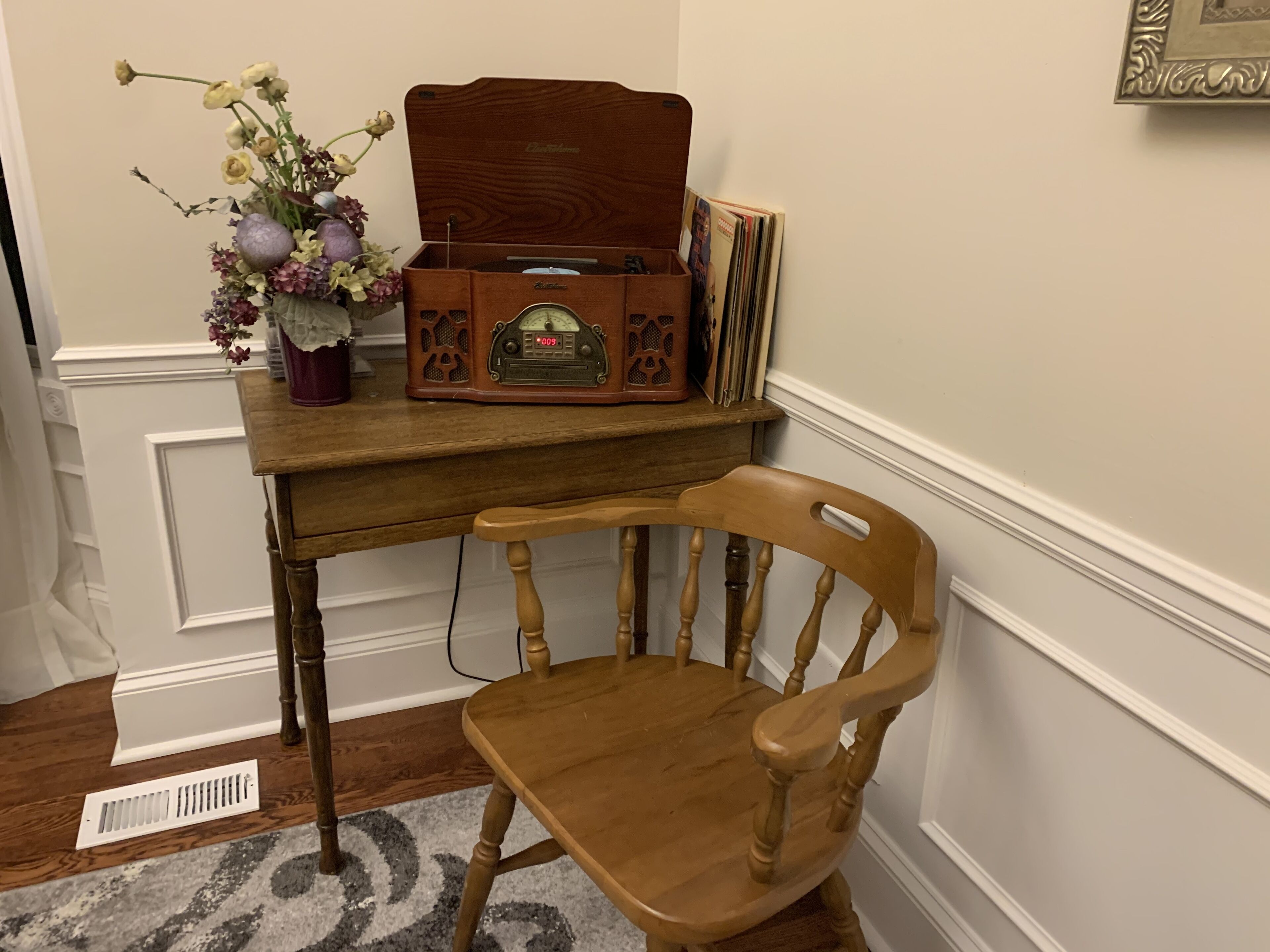 Un bureau en bois, une radio, un vase de fleurs et une chaise.