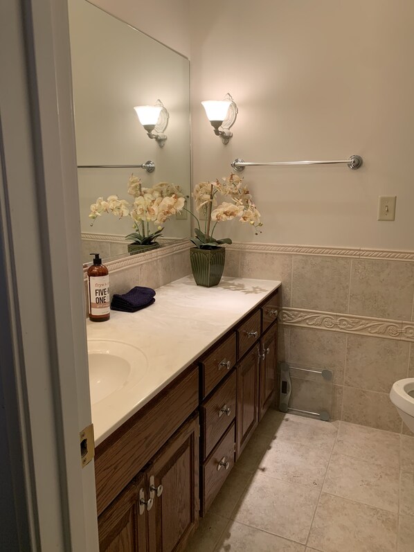 Une salle de bain avec un lavabo blanc, des meubles en bois, une serviette et des orchidées.