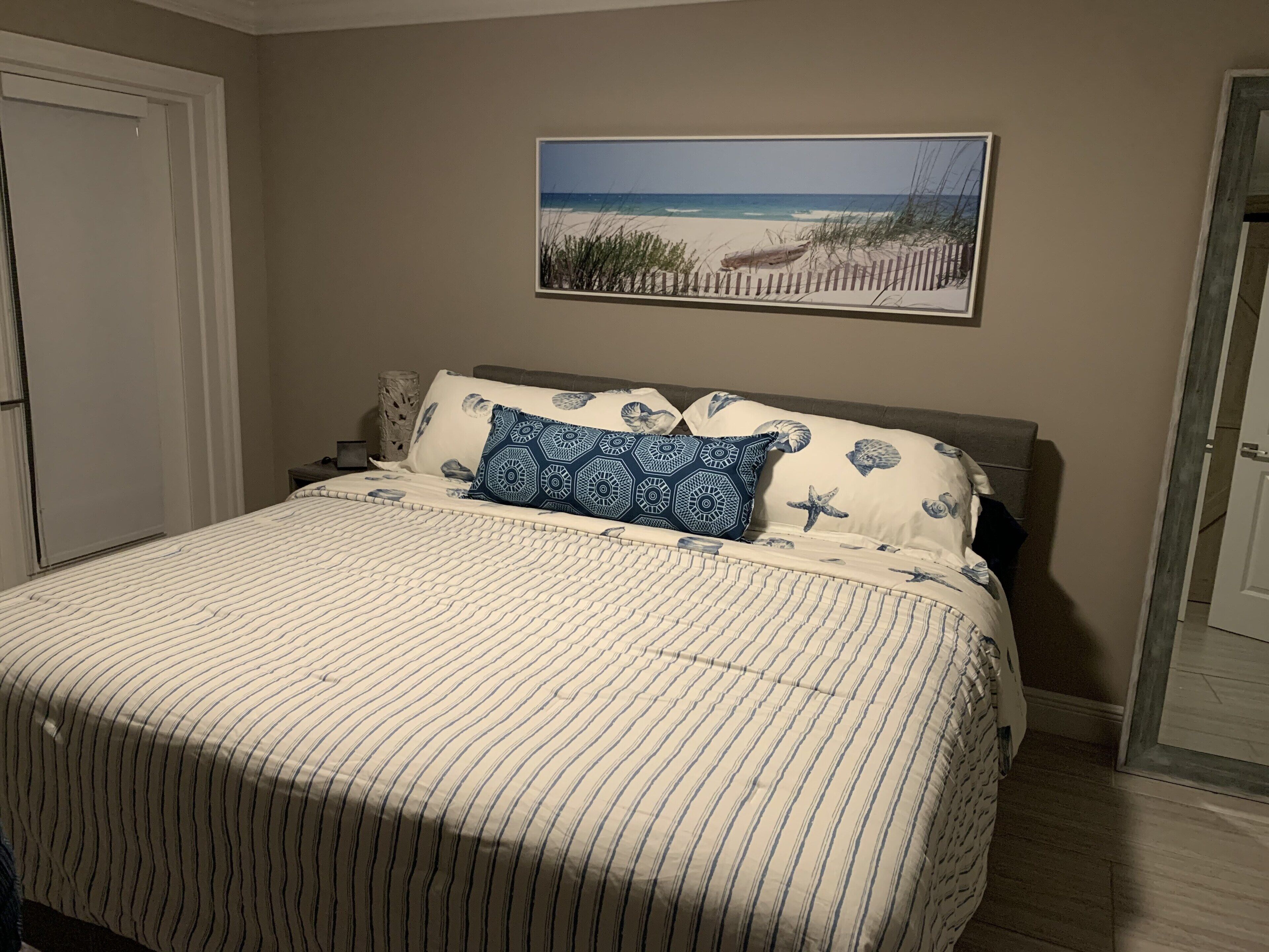 Un dormitorio con una cama, un cuadro de una playa y una puerta.