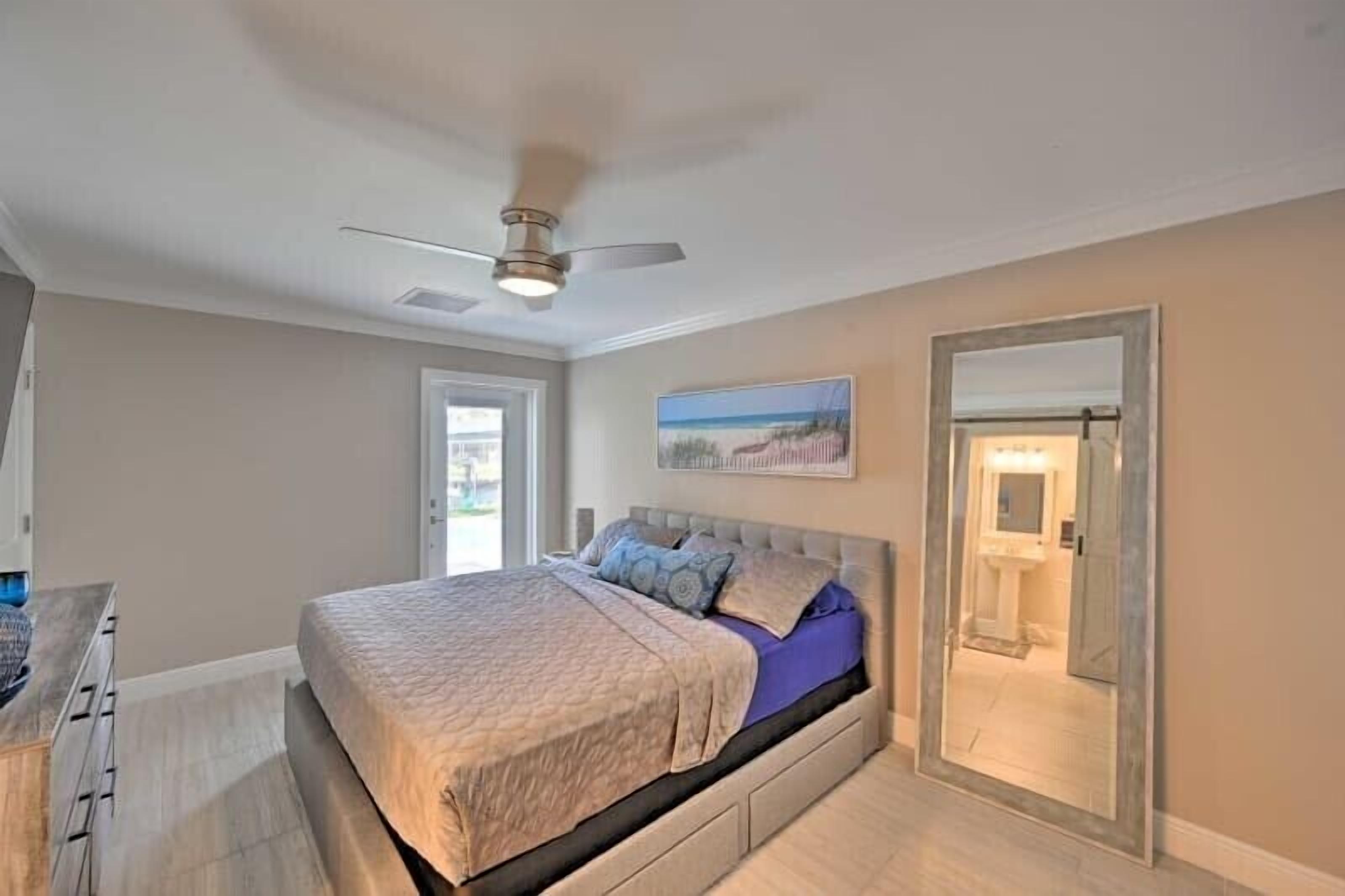 A bedroom with a bed, a ceiling fan, a door, and a painting on the wall.