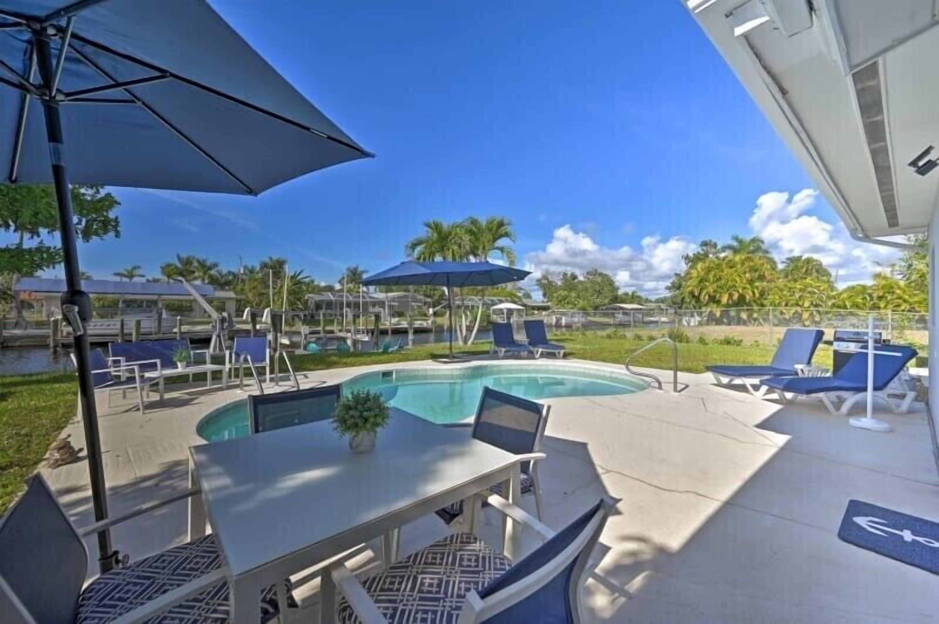 Un espace aménagé au bord de la piscine, avec des chaises longues et des parasols, une table avec des chaises, et une vue dégagée sur la piscine.