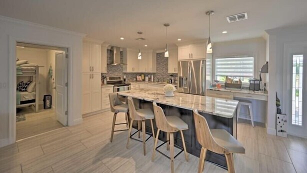 A modern kitchen with a large island, bar stools, and pendant lighting. - Canelas Home, you’re Home away from Home (Cape Coral)