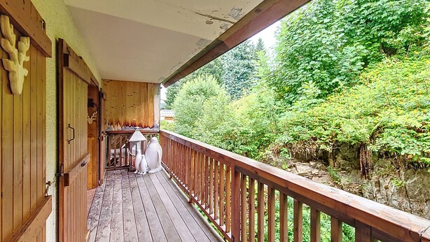 A wooden deck with a railing, leading to a covered porch area with a view of a lush garden.