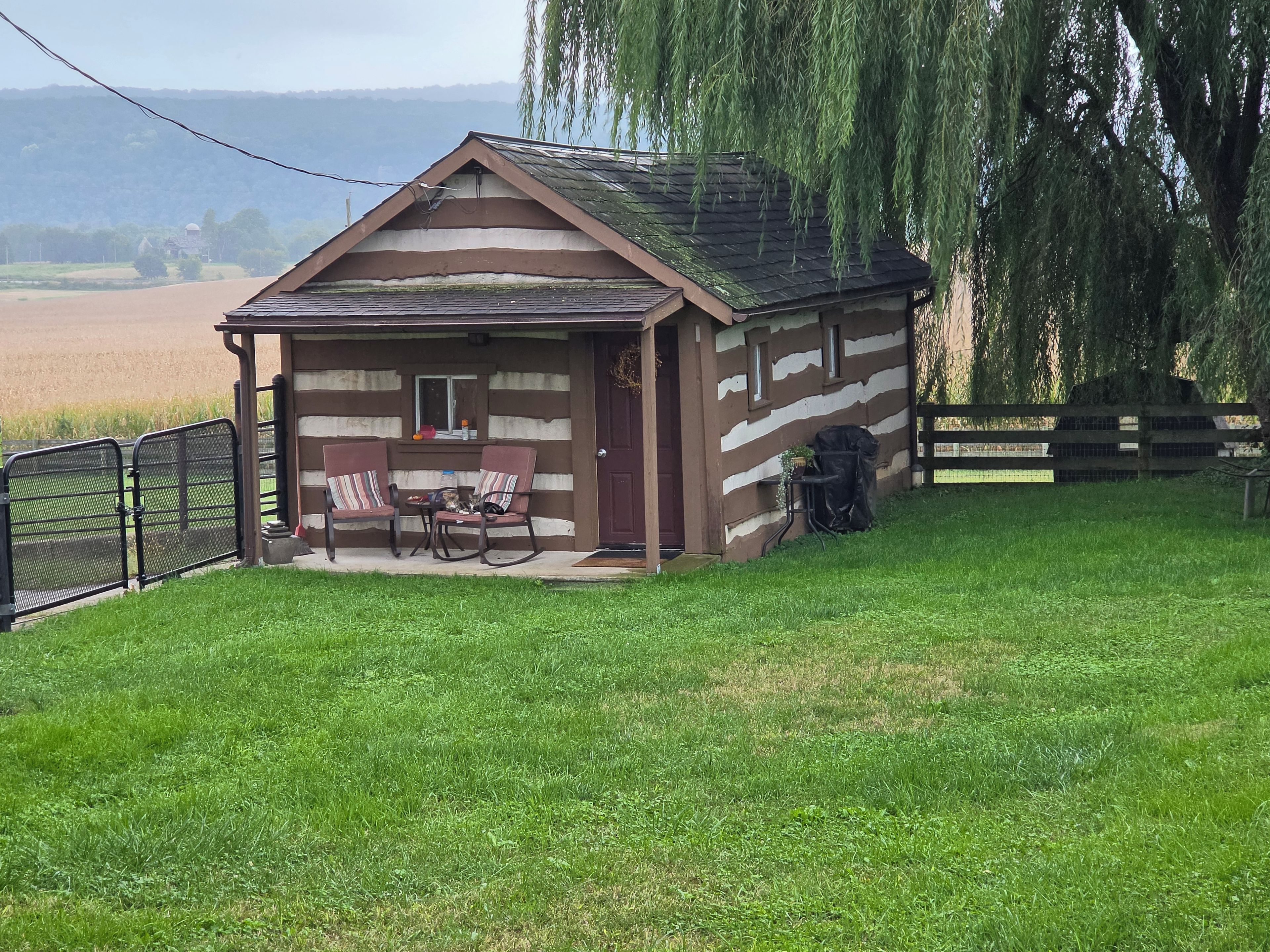 Una pequeña cabaña de madera con un porche, dos mecedoras y una mesa.