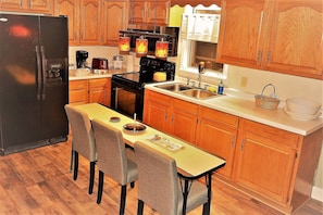 A compact kitchen with wooden cabinets, a black refrigerator, a stove, and a dining table with four chairs.