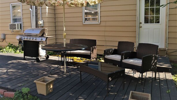 An outdoor patio with a grill, wicker furniture, and a floral umbrella. - The Bungalow: inviting retreat with a spacious backyard sets for BBQs.  (Grand Forks)
