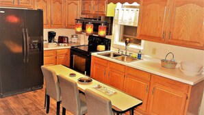 A compact kitchen with wooden cabinets, a black refrigerator, a stove, and a dining table with four chairs. - The Bungalow: inviting retreat with a spacious backyard sets for BBQs.  (Grand Forks)