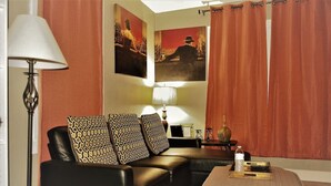 A living room with a black leather sofa, patterned cushions, a wooden coffee table, a floor lamp, and two framed pictures on the wall. - The Bungalow: inviting retreat with a spacious backyard sets for BBQs.  (Grand Forks)