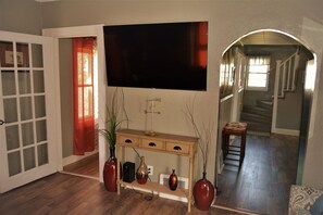 Ein Wohnzimmer mit einem großen Flachbildfernseher an der Wand, einem Holzkonsolentisch mit dekorativen Vasen und einer Treppe, die zu einer anderen Ebene führt.