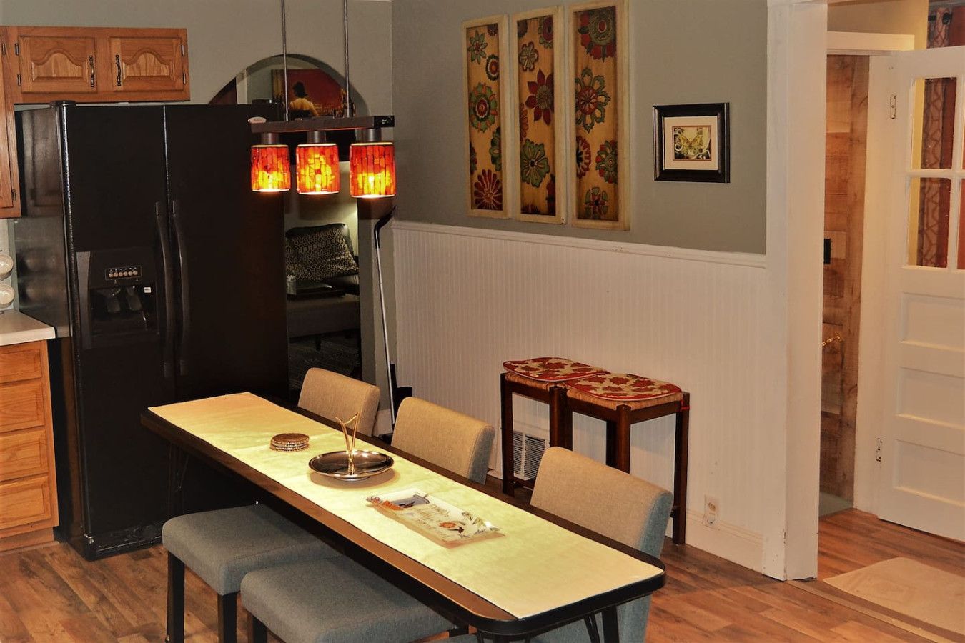 Une cuisine avec un réfrigérateur noir, une table à manger avec des chaises et une petite table d’appoint en bois.