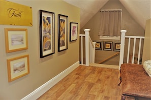 A room with a wooden floor, a staircase, and framed artwork on the walls.