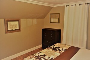 A bedroom with a bed, a dresser, a framed picture on the wall, and a window with curtains.