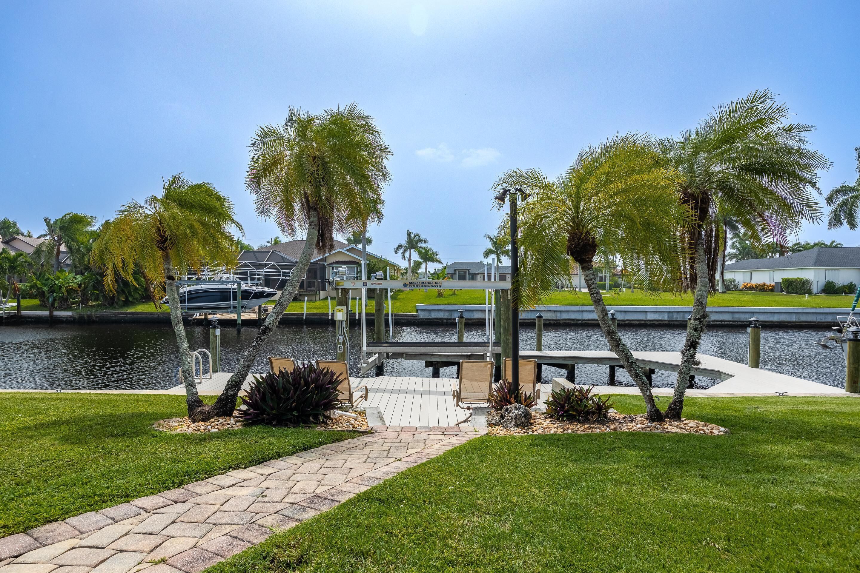 A waterfront property with a dock, palm trees, and a grassy area.