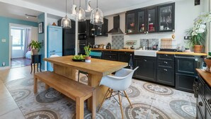 A modern kitchen with dark cabinets, a wooden dining table, and pendant lights. - Appartement Charles - Welkeys (Marseille)