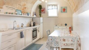 Uma cozinha compacta com teto em arco de pedra, uma mesa de jantar com toalha de mesa estampada e uma janela com vista.