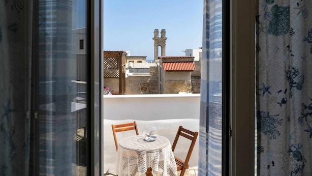 Uma varanda com mesa e cadeiras, vista para edifícios e uma torre ao longe.