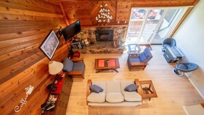 A cozy cabin interior with a stone fireplace, wooden walls, a sofa set, and a television.