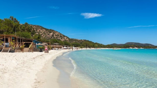 Ein Strand mit klarem türkisblauem Wasser, weißem Sand und einer Holzkonstruktion mit Stufen zum Strand.