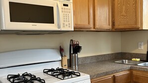 Une cuisine avec des meubles de rangement en bois, un four à micro-ondes blanc, une cuisinière à gaz et un évier en acier inoxydable.