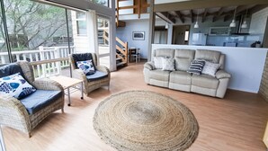 A modern living room with wicker furniture, a beige sofa, and a large window offering a view of the outdoors. - The Outlook - Quiet and Tranquil with Lovely Views (Bermagui)