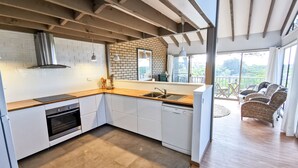A modern kitchen with white cabinets, a wooden countertop, and a built-in oven. There is a large window providing a view of the outdoors. - The Outlook - Quiet and Tranquil with Lovely Views (Bermagui)